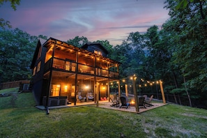 A two-story wooden cabin with a balcony, string lights, and outdoor seating.