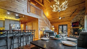 A wooden cabin interior with a dining area, kitchen, and a stone fireplace. - Private Hiking Trail, Full Game Rm, Great Location (Morganton)