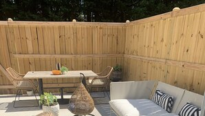 A patio area with a wooden table, wicker chairs, a sofa, and a patterned rug.