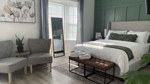 A modern bedroom with a large bed, a mirror, a gray sofa, and a potted plant.