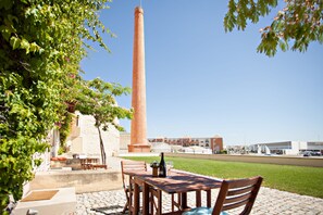 A patio with a brick table and chairs, a bottle of wine, and a view of a tall brick chimney and modern buildings in the background. - Historic & Emblematic - Convent of Bernardas (Tavira)