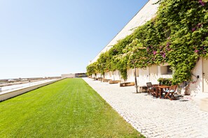 A row of outdoor seating with a view of the sea, a grassy area, and a building with climbing plants. - Historic & Emblematic - Convent of Bernardas (Tavira)