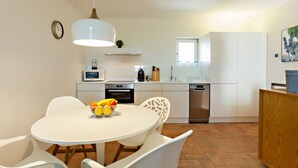 A modern kitchen with white cabinetry, a dining table with chairs, a microwave, and a sink. - Historic & Emblematic - Convent of Bernardas (Tavira)