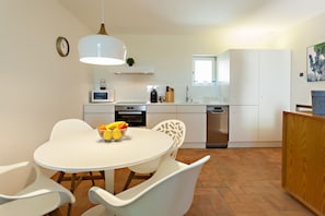 A modern kitchen with white cabinetry, a dining table with chairs, a microwave, and a sink. - Historic & Emblematic - Convent of Bernardas (Tavira)