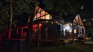 Une cabane dotée d’une grande terrasse, d’un porche abrité et d’un intérieur visible, avec une cheminée.
