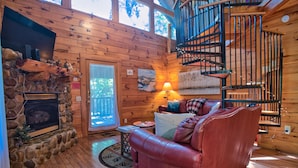 Un intérieur de chalet chaleureux avec une cheminée en pierre, des murs en bois, un canapé en cuir et un escalier en colimaçon.
