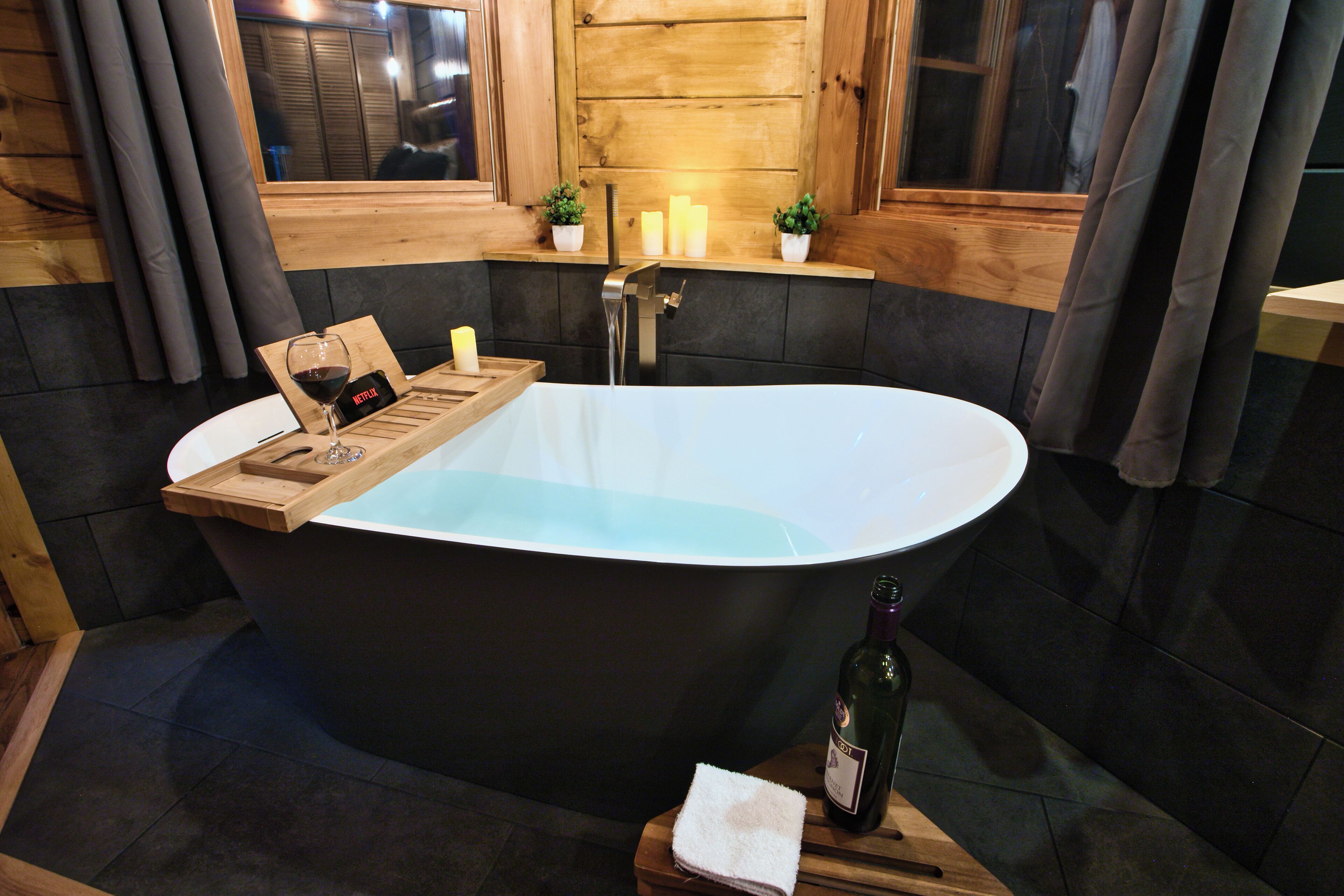A modern bathroom with a freestanding bathtub, wooden accents, and a window with curtains.