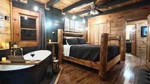 Une chambre à coucher de style cabane en bois, avec un grand lit, un bureau en bois, une baignoire et un ventilateur de plafond.