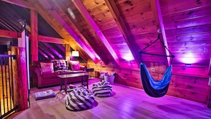 Une chambre confortable située sous les toits, avec des poutres en bois, un hamac, des fauteuils en forme de sac et un canapé rouge.