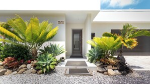 A modern villa with a sign reading "MAMA TARA'S 4 LUXURY VILLA," featuring a gravel driveway, tropical plants, and a minimalist entrance. - Mama Taras Luxury Villa (Rarotonga)