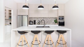A modern kitchen with a central island, bar stools, pendant lighting, and built-in appliances. - Mama Taras Luxury Villa (Rarotonga)