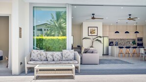 A modern living room with a sofa, coffee table, and a large window with a view of palm trees. - Mama Taras Luxury Villa (Rarotonga)
