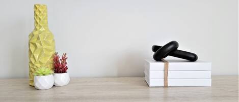 A wooden shelf with a yellow vase, two small potted plants, and a stack of white boxes with a black object on top.