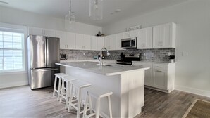 A modern kitchen with white cabinetry, a stainless steel refrigerator, a built-in oven, and a large island with bar stools. - ♡ Beautiful Modern & Luxury Beach Home Next to Boardwalk With Bay View (Ocean City)