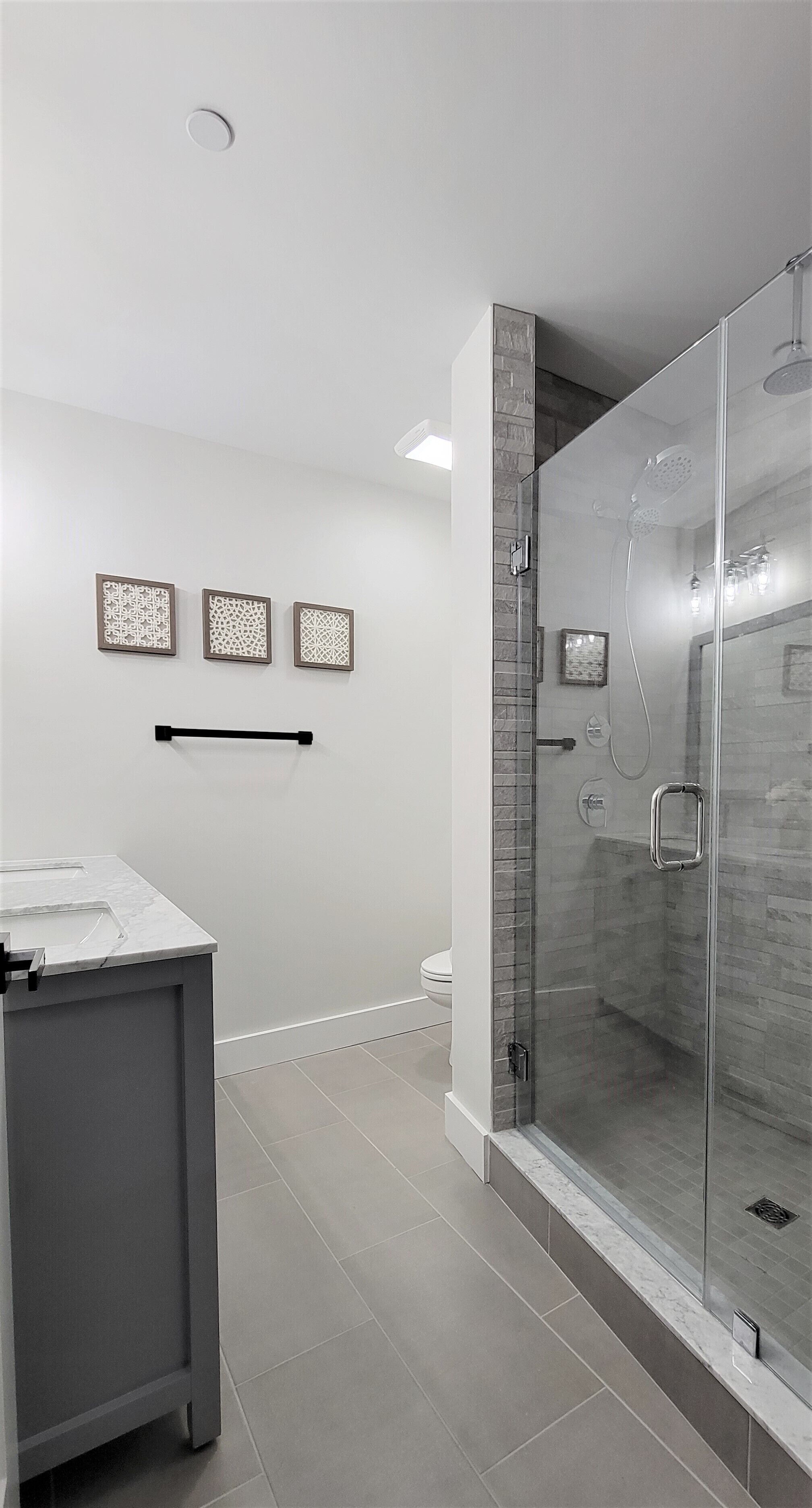 Een moderne badkamer met een douchecabine van glas, een marmeren wastafel en drie decoratieve wandpanelen.