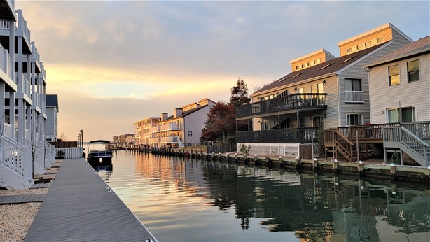 A waterfront property with a dock, buildings with balconies, and a boat docked at the pier. - ♡ Beautiful Modern & Luxury Beach Home Next to Boardwalk With Bay View (Ocean City)