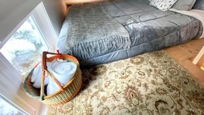 A bedroom with a bed, a patterned rug, a basket with towels, and a window with a view. - Ski In Ski out Cozy Condo in Creekside forest (Whistler)