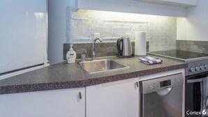 A modern kitchen with white cabinets, a granite countertop, stainless steel appliances including a dishwasher, oven, and stove, and a tiled backsplash. - Ski In Ski out Cozy Condo in Creekside forest (Whistler)