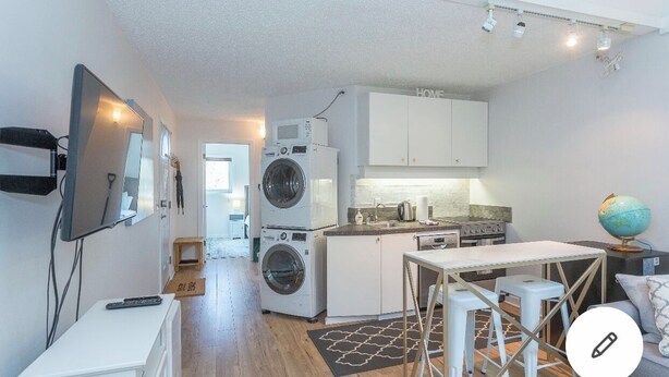 A compact apartment with a kitchenette, a washing machine, a TV mounted on the wall, and a globe on a side table. - Ski In Ski out Cozy Condo in Creekside forest (Whistler)