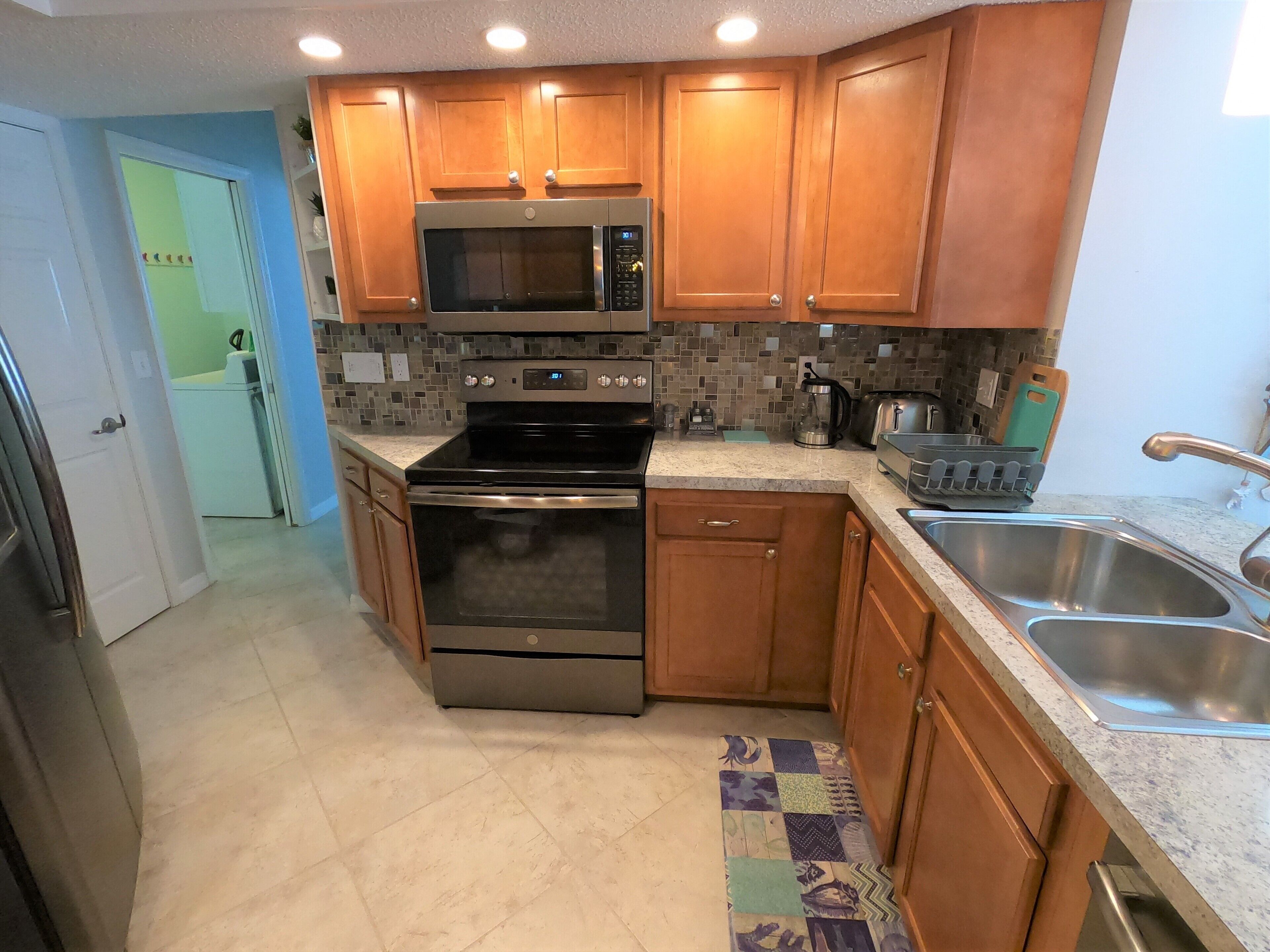 A kitchen with wooden cabinets, a stainless steel sink, a microwave, an oven, and a coffee maker.