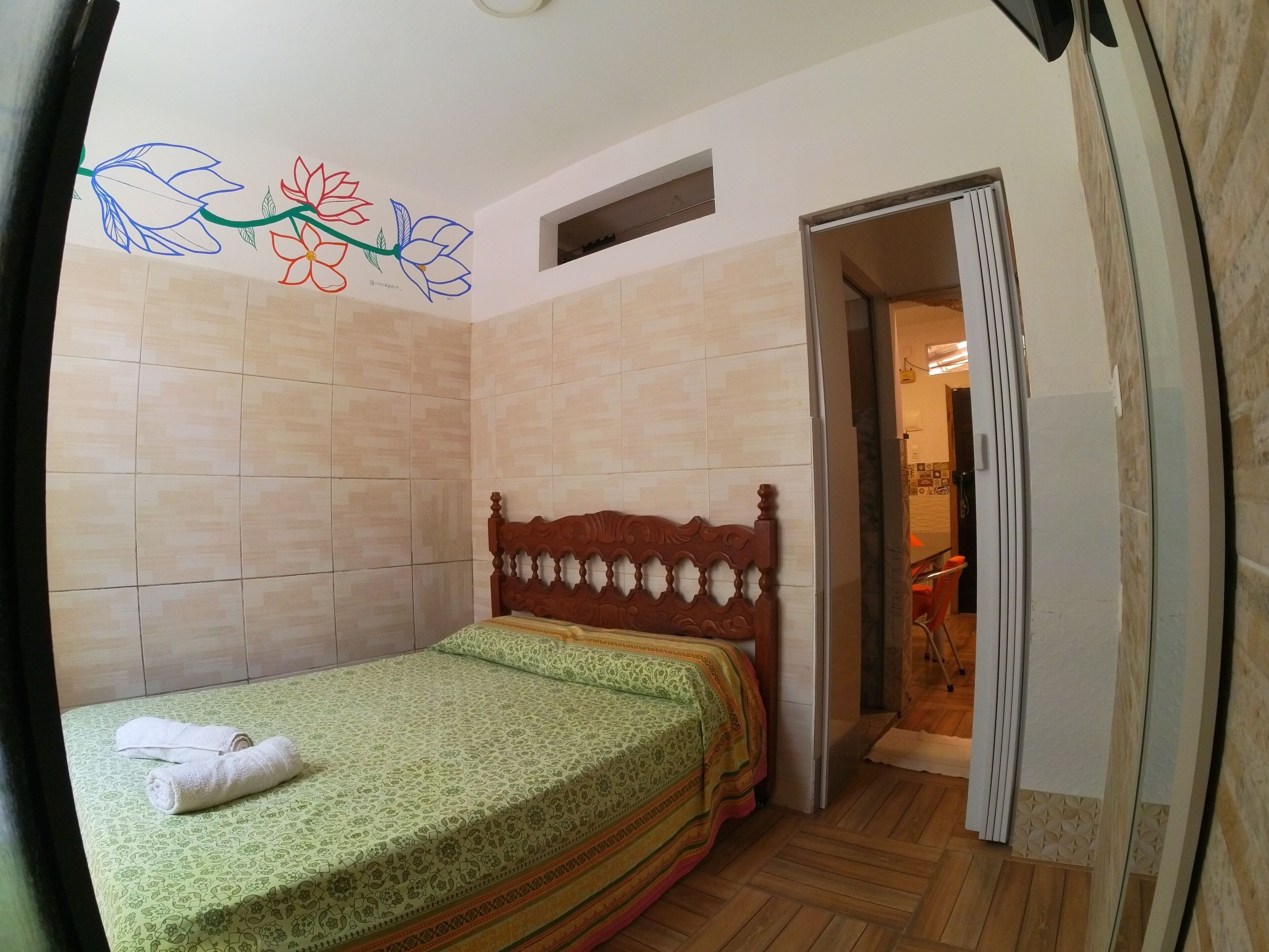 Una habitación con cama, cabecera de madera, pared con un mural floral y suelo de baldosas.