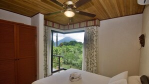 Un dormitorio con cama, ventilador de techo, vista de una montaña a través de una ventana y un armario de madera.