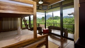 Una habitación con una cama litera de madera, ventilador de techo, televisión y balcón con vistas a zonas verdes y montañas.