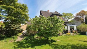 Une maison d’habitation avec un jardin, un chemin et une personne debout dans la cour.