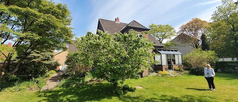 A residential house with a garden, a pathway, and a person standing in the yard.