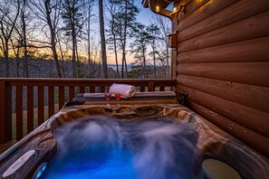 Un bain à remous sur une terrasse en bois, avec vue sur les arbres et un coucher de soleil.