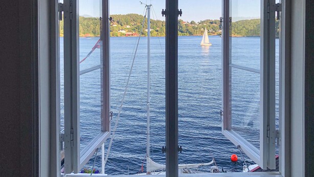 A view from a window overlooking a body of water with a sailboat and a wind turbine in the distance. - Stunning apartment in Arendal with WiFi (Arendal)