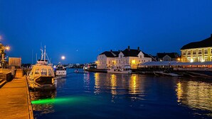 A waterfront marina at dusk with boats docked, a building with a sign 'AMIGA', and a large illuminated structure on the right. - Stunning apartment in Arendal with WiFi (Arendal)