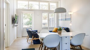 Un coin repas moderne avec une table blanche, quatre chaises et une grande fenêtre donnant sur la verdure.
