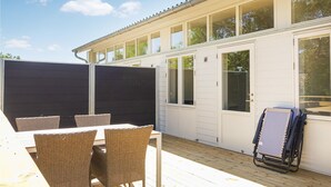 Un espace extérieur abrité, équipé d’une table et de chaises, d’un barbecue et d’un fauteuil roulant.
