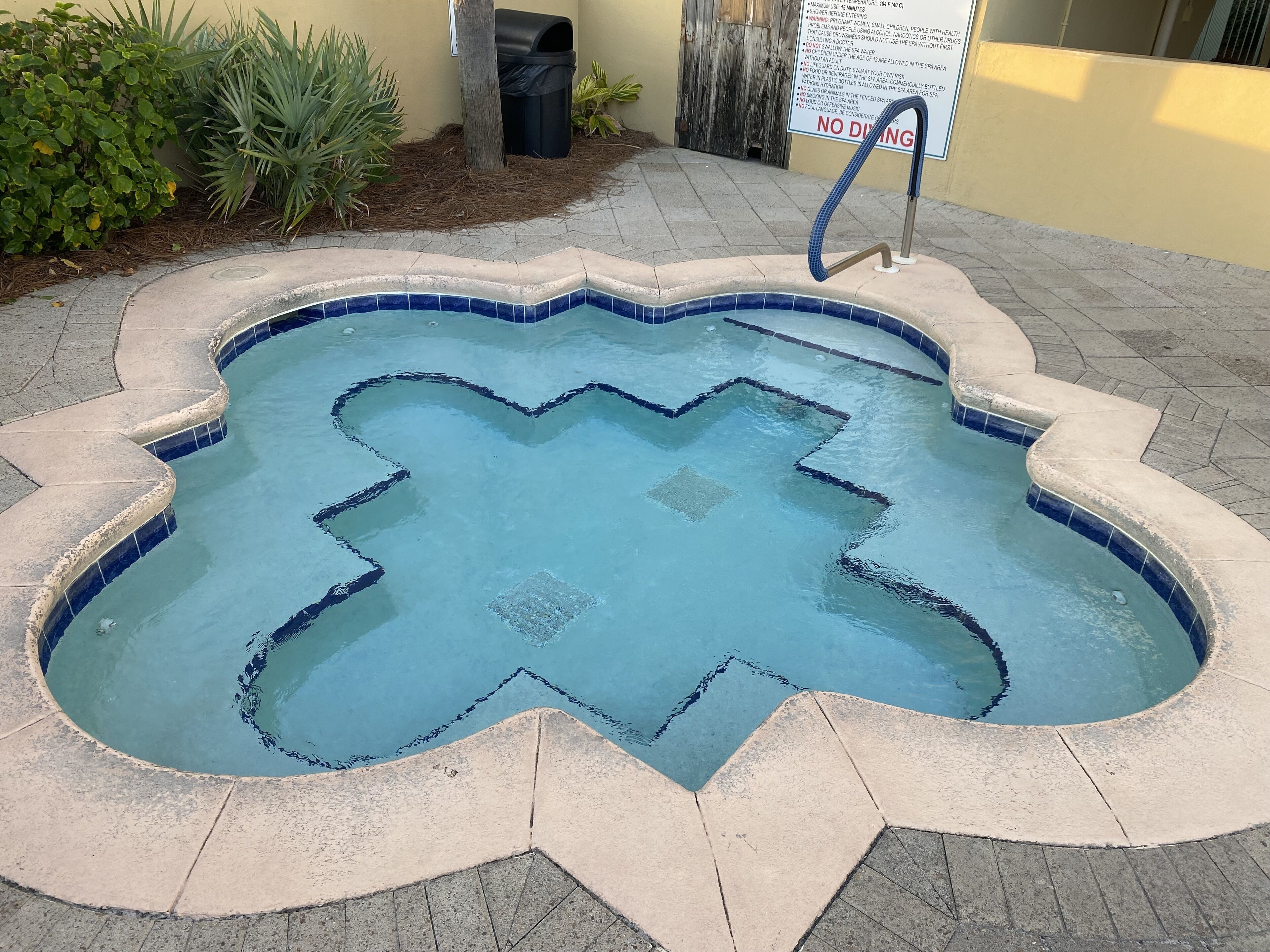 A heart-shaped pool with a tiled edge, surrounded by a concrete deck and a sign prohibiting diving.