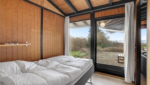 A bedroom with a bed, wooden walls, a window, and a view of the outdoors.