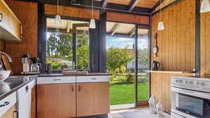 A modern kitchen with wooden cabinets, a built-in oven, and a large window offering a view of a green garden.