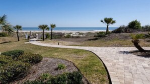 A paved pathway leading to a beach with palm trees and a wooden structure. - Sandcastle Court #277 -Kitchen (Fernandina Beach)