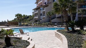 A swimming pool with lounge chairs, palm trees, and a multi-story building in the background. - Sandcastle Court #277 -Kitchen (Fernandina Beach)