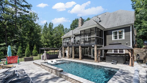 Una casa moderna con piscina, mobiliario exterior y un patio cubierto.