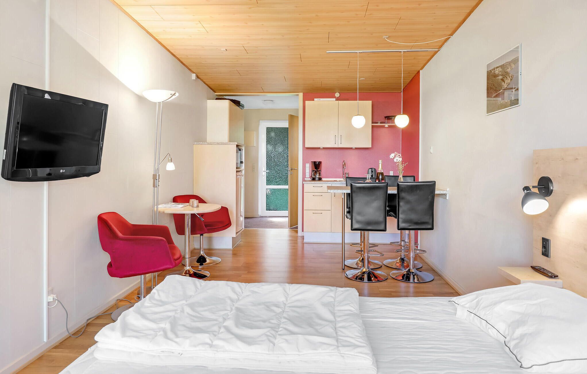 Habitació d'hotel compacta amb llit, escriptori, cadira, televisió i petita cuina.