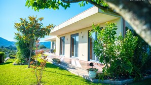 Ett modernt hus med en inglasad veranda, omgivet av frodig grönska och en klarblå himmel.