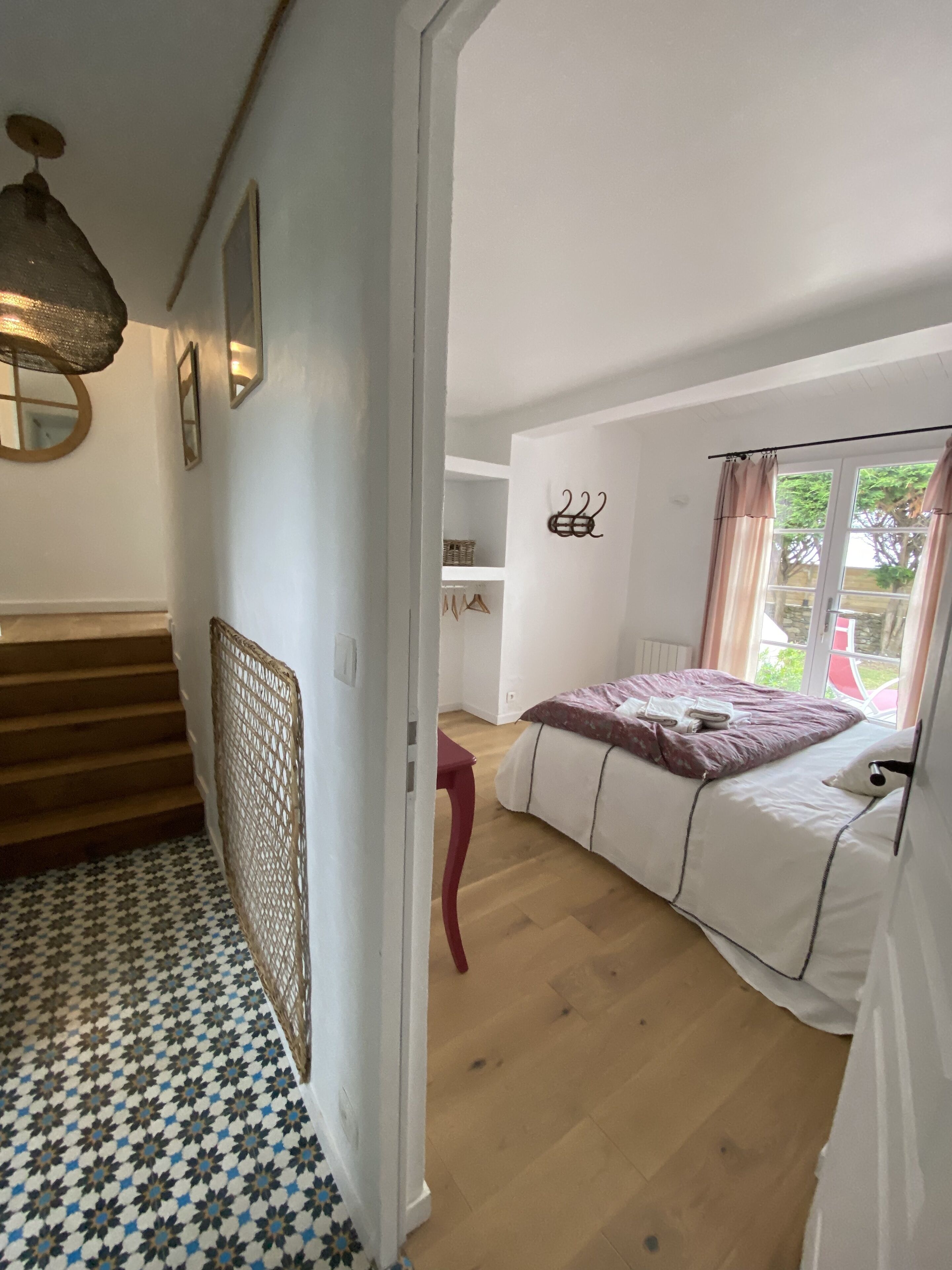 Une chambre à coucher avec un lit, une fenêtre avec des rideaux, un plancher en bois et un escalier menant à une autre pièce.