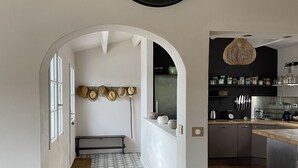 A modern kitchen with a large wall clock, wooden flooring, and a bench in the hallway.