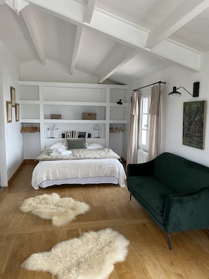 A bedroom with a bed, a green sofa, a wooden floor, a white ceiling, and a painting on the wall.