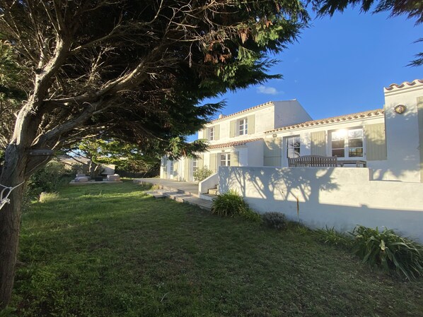 A two-story house with a white exterior and green shutters, a front porch, and a well-maintained lawn.