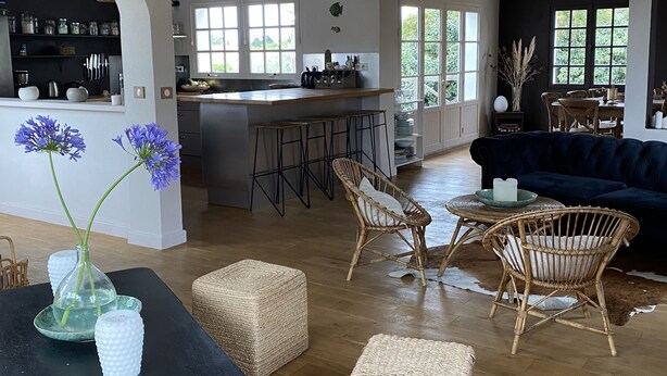 A spacious living area with a dining table, wicker furniture, and a large clock on the wall.