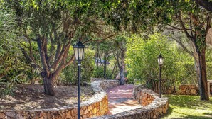 A stone pathway leading through a garden with trees and two street lamps. - Beautiful apartment in Porto Cervo (Porto Cervo)