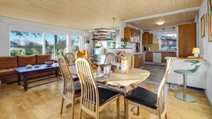 Une cuisine moderne avec des meubles en bois, un coin repas avec une table ronde et des chaises, et un salon avec un canapé et une table basse.