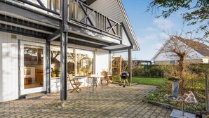 Une maison moderne dotée d’un patio comprenant une table et des chaises, un barbecue et un jardin agrémenté d’un abreuvoir pour oiseaux.